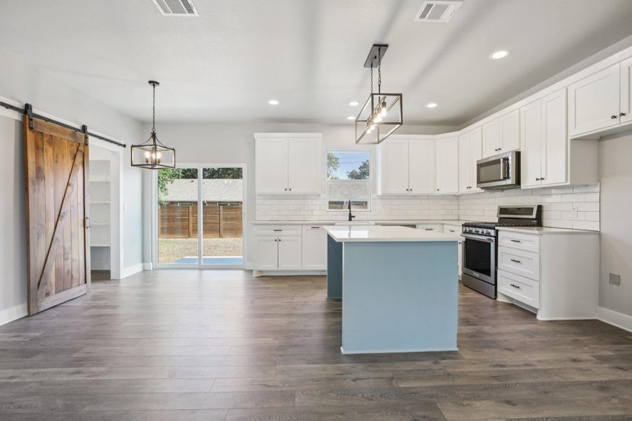 Kitchen with pendant lighting, appliances with stainless steel finishes, white cabinets, dark wood-style flooring, and backsplash