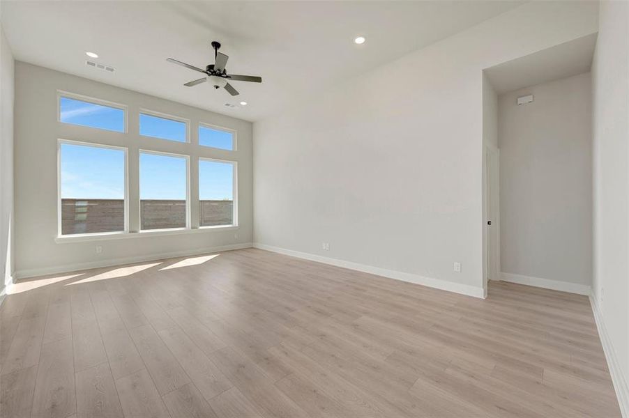 Spacious room featuring light wood-finish flooring, high ceilings, and recessed lighting