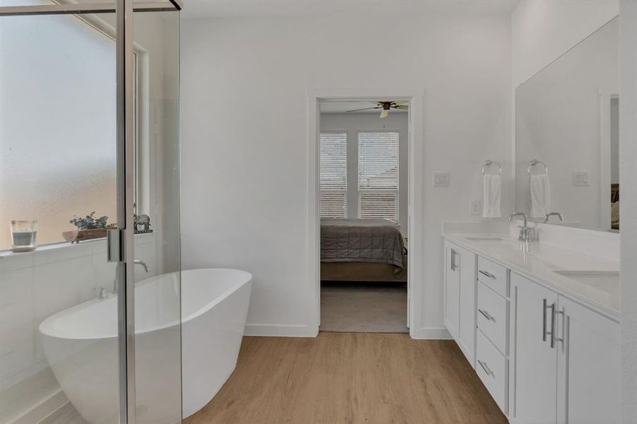Bathroom featuring light wood finished floors, double vanity, ensuite bathroom, a soaking tub, and a ceiling fan