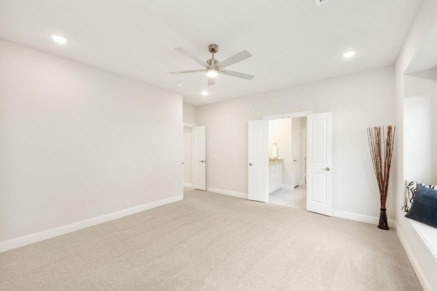 Spacious bedroom with carpet, ceiling fan, and open ensuite bathroom door