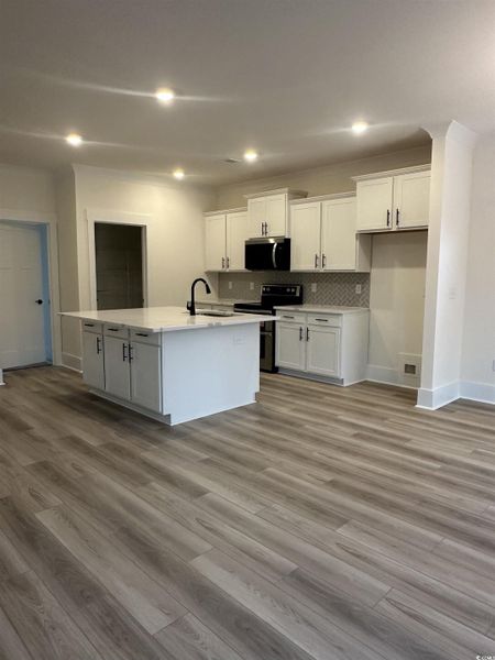 Kitchen featuring white cabinetry, appliances with stainless steel finishes, recessed lighting, decorative backsplash, and a center island with sink