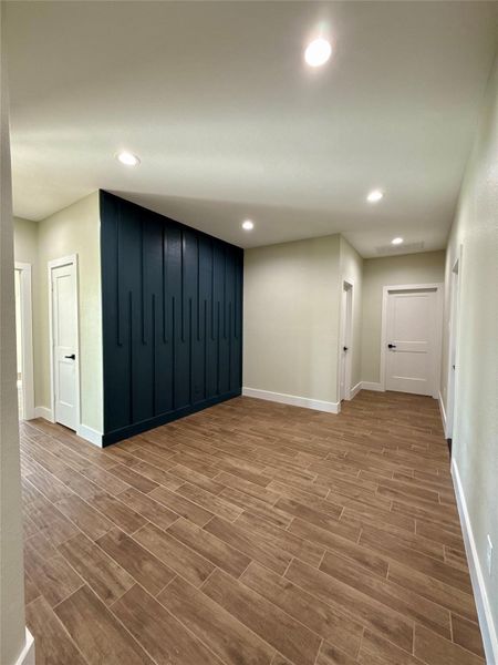 This hallway features modern recessed lighting, wood-style tiled flooring, and a striking dark accent wall. Multiple doors lead to different rooms, offering functional and aesthetic appeal. This hallway features modern recessed lighting, wood-style tiled flooring, and a striking dark accent wall. Multiple doors lead to different rooms, offering functional and aesthetic appeal.