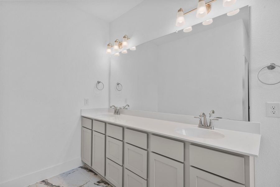 A dual vanity with ample counter space and elegant cabinetry provides plenty of room for two, with a large mirror and modern lighting that make the space feel bright and open. A dual vanity with ample counter space and elegant cabinetry provides plenty of room for two, with a large mirror and modern lighting that make the space feel bright and open.