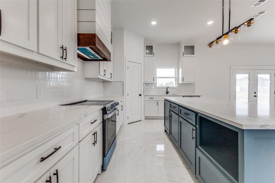 Kitchen featuring backsplash, white cabinets, electric range, decorative light fixtures, and light stone counters