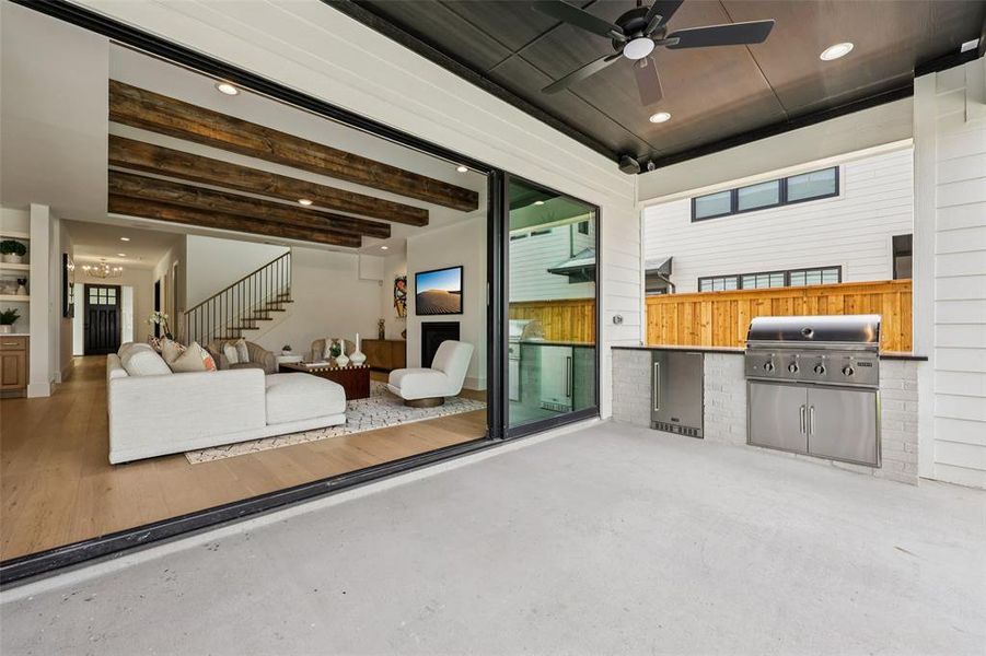 Covered patio featuring an outdoor kitchen with a built-in stainless steel grill and refrigerator, an overhead ceiling fan, and sliding glass doors opening to the interior living space