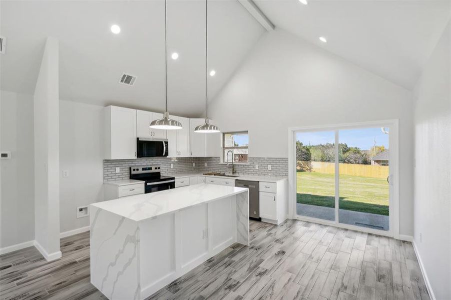 Kitchen with light stone countertops, a center island, stainless steel appliances, pendant lighting, and white cabinets