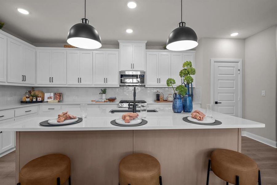 Kitchen featuring light wood finished floors, stainless steel appliances, a center island with sink, and hanging light fixtures