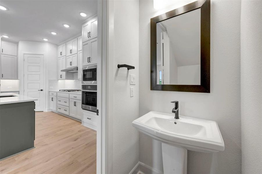 Pedestal sink with a dark framed mirror and wall-mounted light fixture Pedestal sink with a dark framed mirror and wall-mounted light fixture