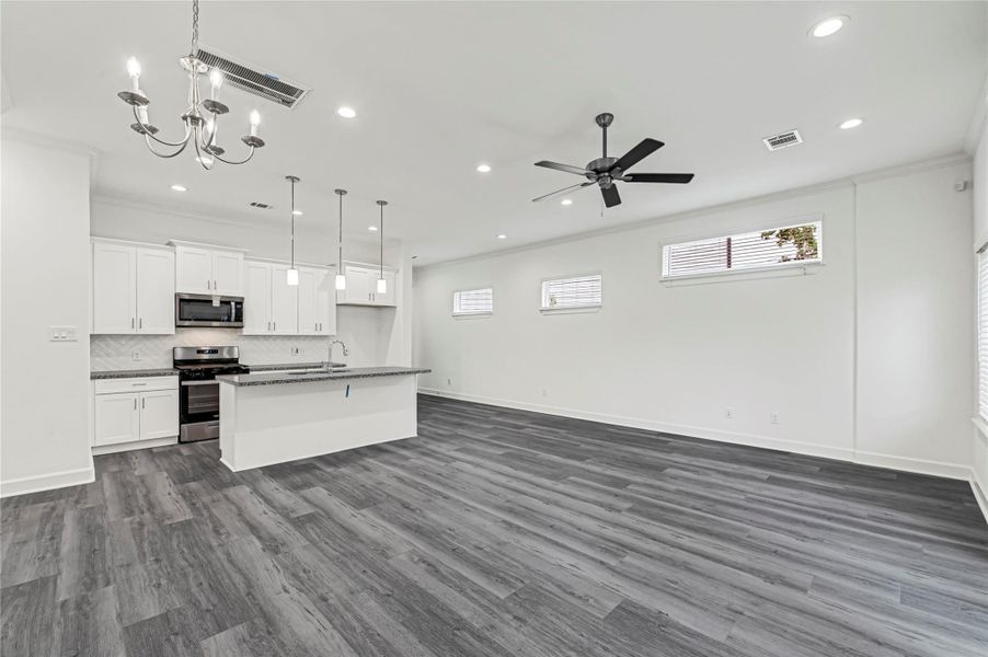 This photo showcases a modern, open-concept living space with a sleek kitchen featuring white cabinetry, stainless steel appliances, and a large island. The room is well-lit with recessed lighting, a ceiling fan, and offers stylish gray flooring, creating a bright and inviting atmosphere. This photo showcases a modern, open-concept living space with a sleek kitchen featuring white cabinetry, stainless steel appliances, and a large island. The room is well-lit with recessed lighting, a ceiling fan, and offers stylish gray flooring, creating a bright and inviting atmosphere.