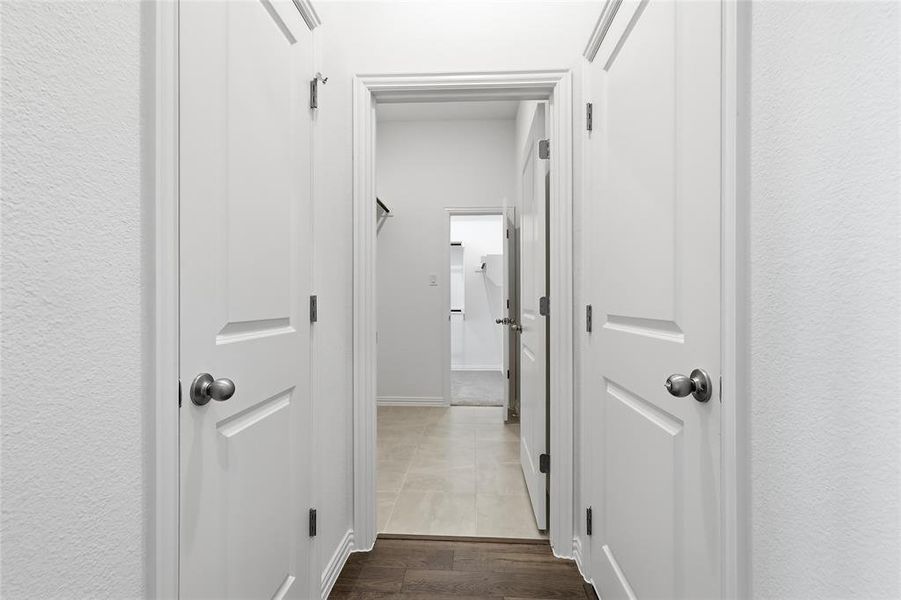 Hallway featuring white paneled doors with brushed nickel hardware, light-colored textured walls, and a contrasting wood-finish floor at the foreground