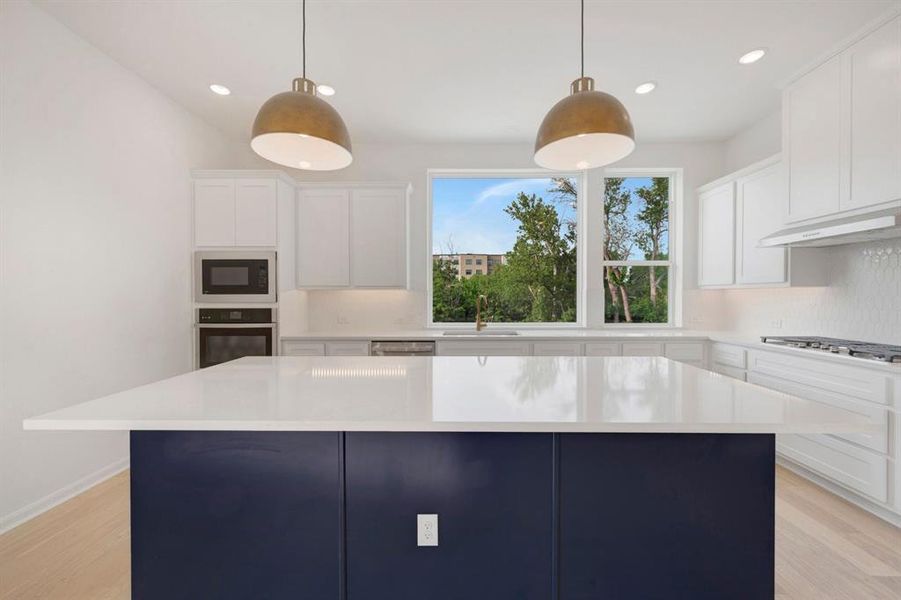 Kitchen featuring an expansive center island with a stone countertop, white upper and lower cabinetry, and stainless steel appliances