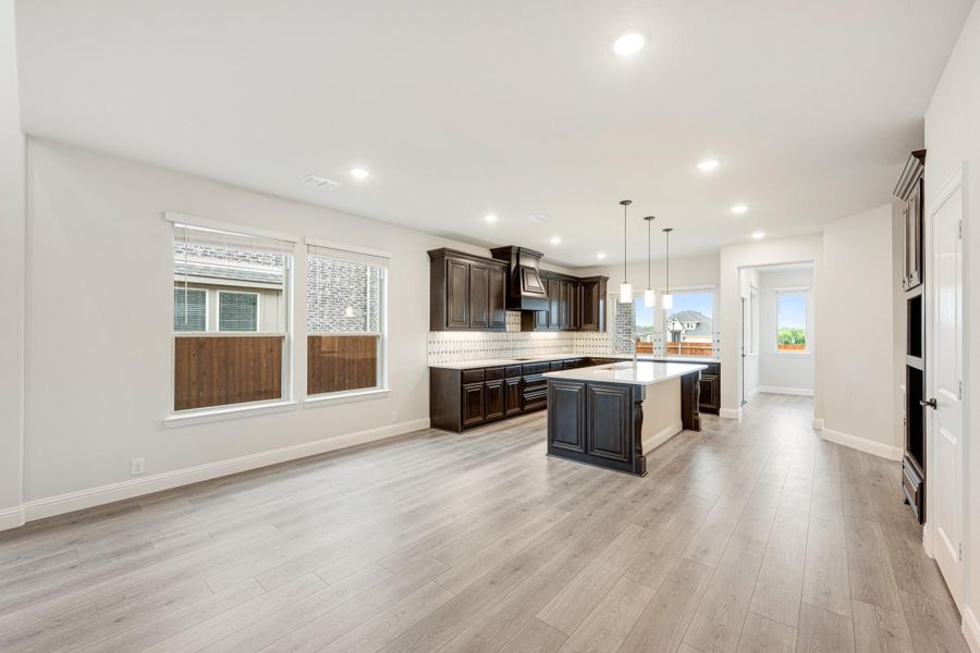 Open kitchen with dark wood cabinets, center island, pendant lights, and light hardwood floors