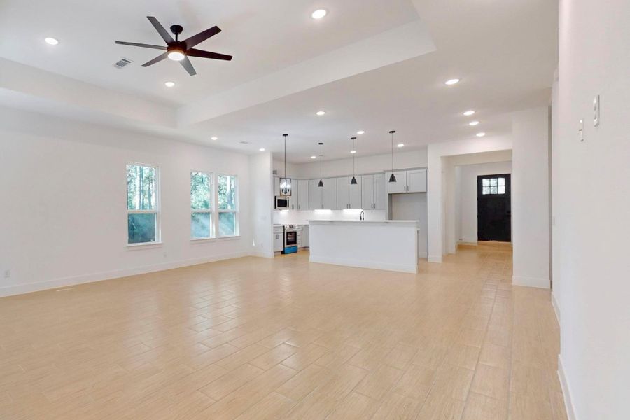 Unfurnished living room with light wood-type flooring, a ceiling fan, recessed lighting, and a tray ceiling