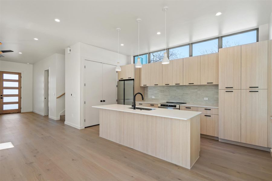 Kitchen with light brown cabinets, stainless steel appliances, a sink, backsplash, and modern cabinets