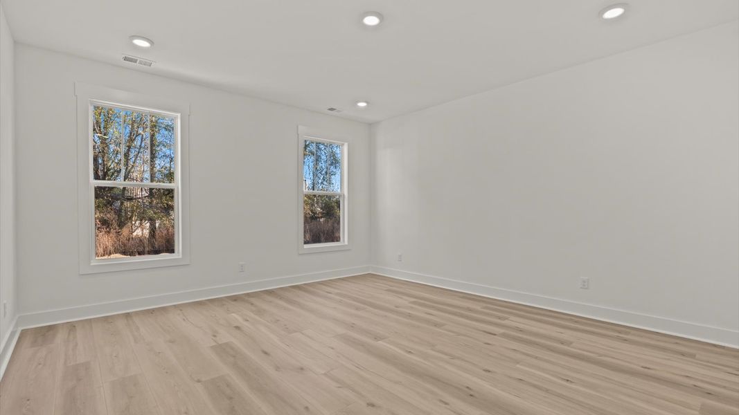 Elegant primary suite with hardwood flooring and superior natural light in this accomplished DRB Homes design