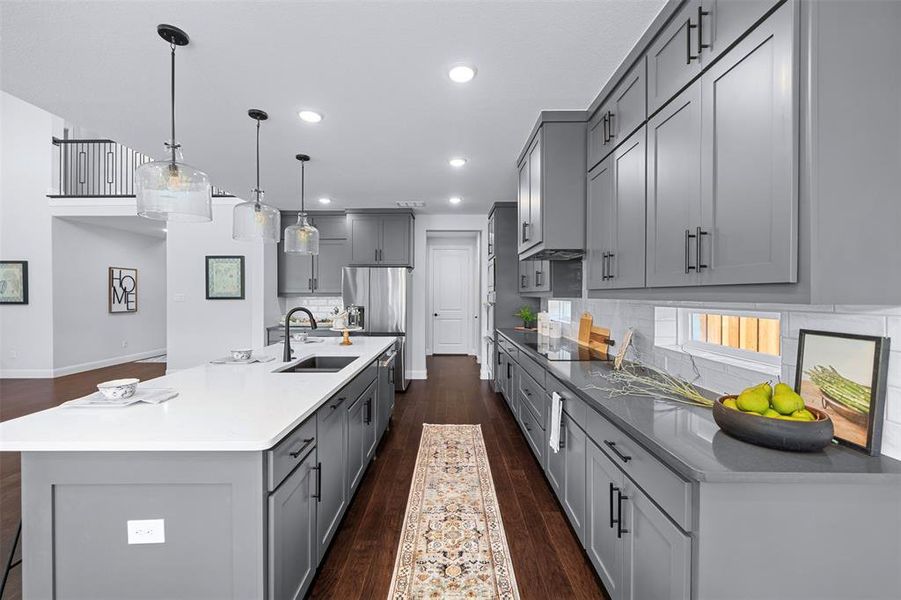 Kitchen featuring decorative backsplash, gray cabinetry, dark wood-style floors, an island with sink, and hanging light fixtures