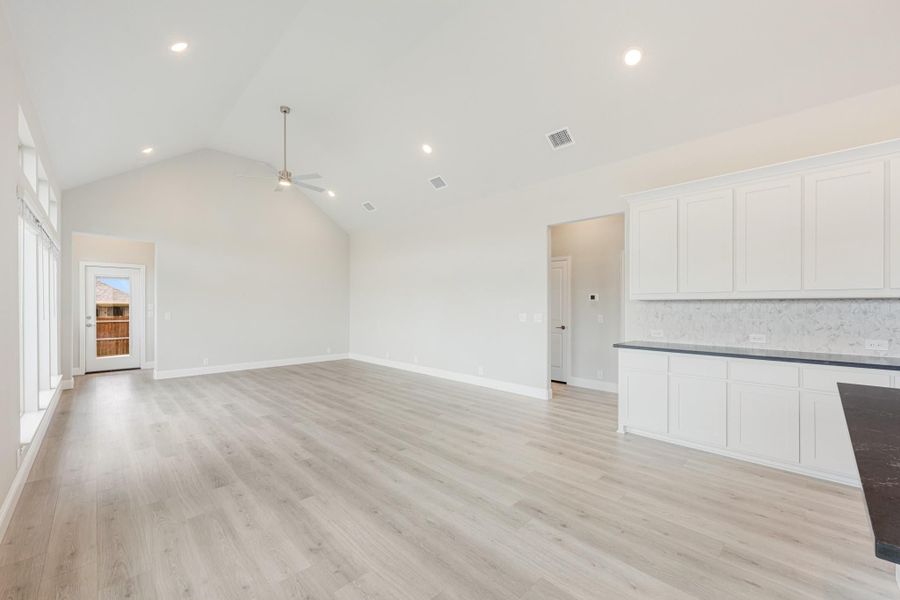 Open living area with vaulted ceiling, light wood floors, and white kitchen cabinets with dark countertops