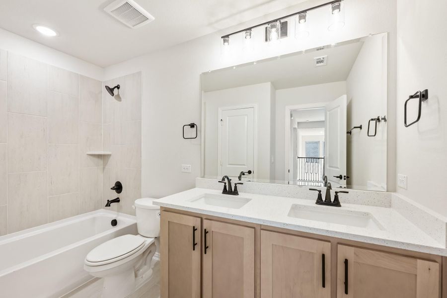 Bathroom with double sink vanity, large mirror, soaking tub, and tiled shower surround with black fixtures