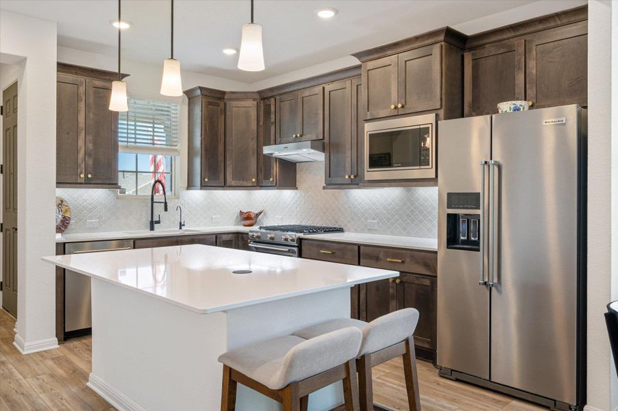 Kitchen with high end appliances, dark wood finish cabinets, decorative light fixtures, and light wood finished floors Kitchen with high end appliances, dark wood finish cabinets, decorative light fixtures, and light wood finished floors
