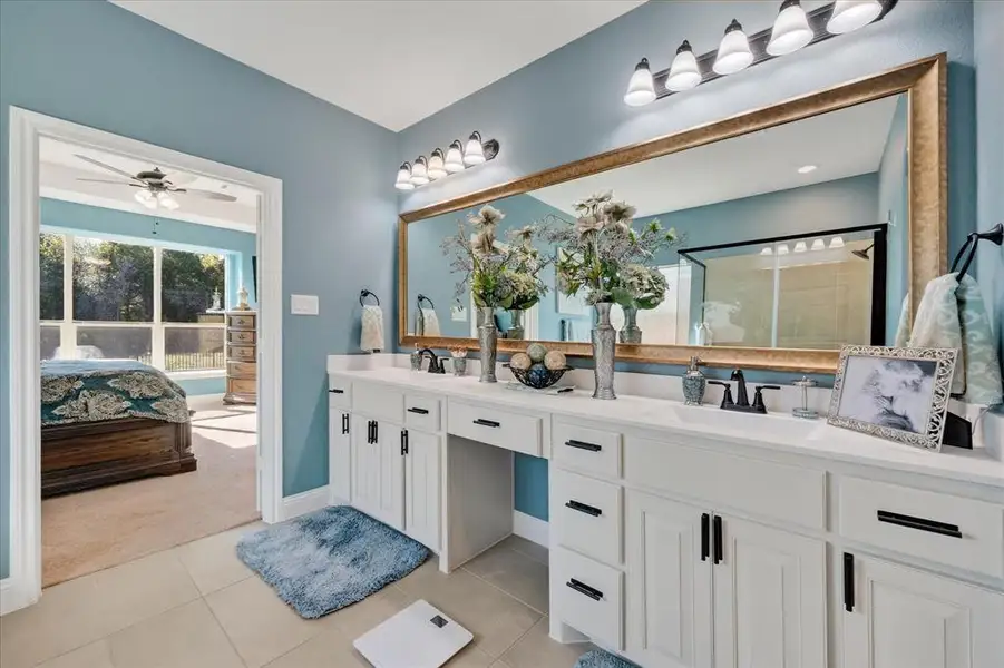 Ensuite bathroom featuring double vanity, light tile patterned floors, tiled shower, and a ceiling fan Ensuite bathroom featuring double vanity, light tile patterned floors, tiled shower, and a ceiling fan