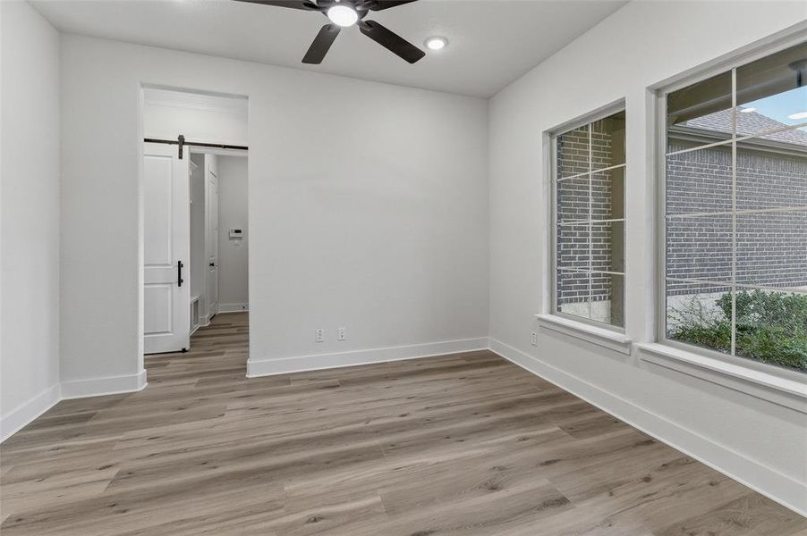 Spacious room featuring wood-finish flooring, white walls, and a ceiling fan with integrated lighting Spacious room featuring wood-finish flooring, white walls, and a ceiling fan with integrated lighting