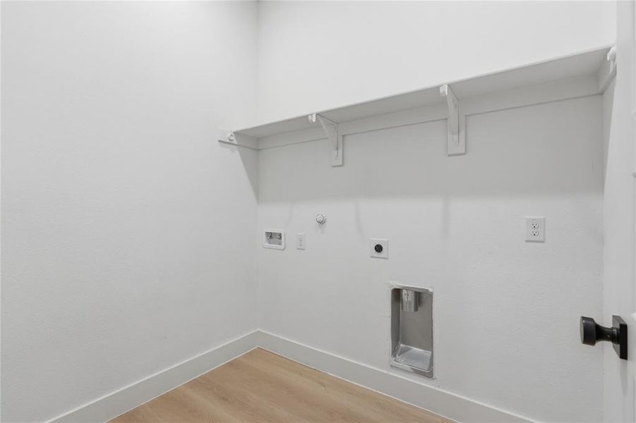 Dedicated utility space featuring a built-in shelf, light wood-finish flooring, white baseboards, and a black door handle