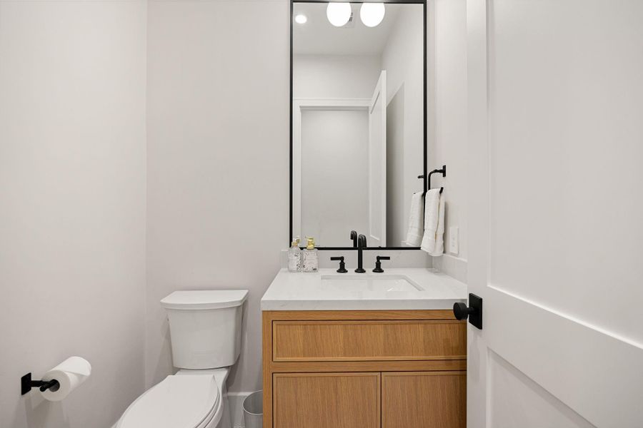A sleek and functional powder room designed with modern appeal, featuring warm wood cabinetry, a crisp white countertop, and matte black fixtures. Clean lines and minimal design create a sophisticated look. The highlight of this space is the striking contrast between the wood vanity and bold black hardware, adding depth and contemporary style to this compact yet impactful room.