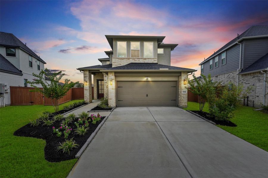 The home boasts a thoughtful, two-story design and a beautifully landscaped front yard. The warm glow of the exterior lighting highlights the home's striking curb appeal as dusk settles.