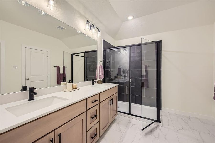Full bath featuring a shower stall, double vanity, vaulted ceiling, and light marble finish flooring