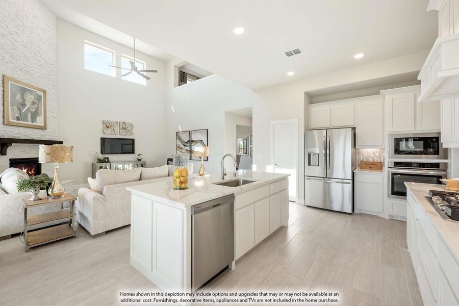 Open-concept kitchen with white island, stainless appliances, and adjoining living room with stone fireplace