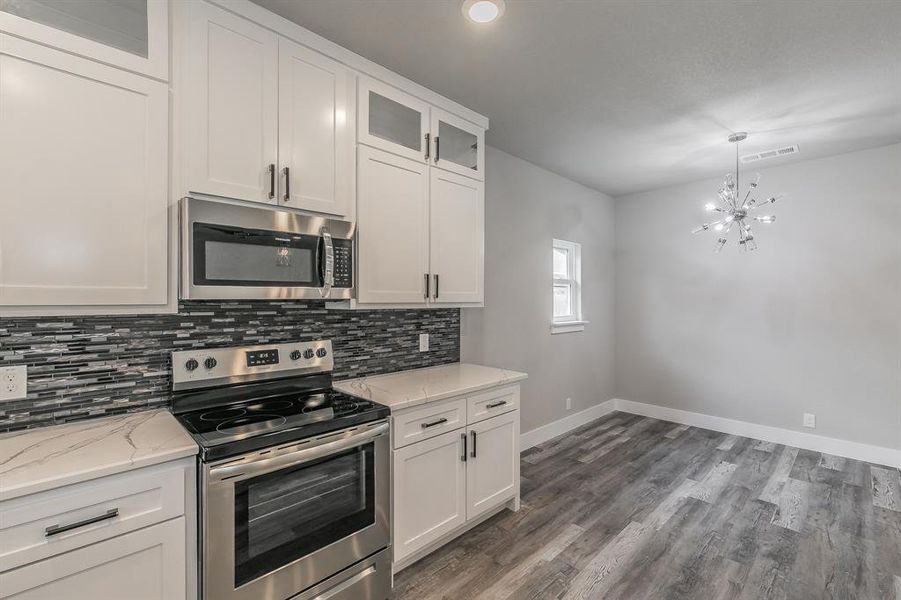 Kitchen with dark hardwood / wood-style floors, a chandelier, white cabinetry, and appliances with stainless steel finishes