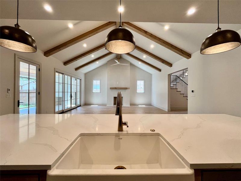 Kitchen with light stone countertops, hardwood / wood-style floors, hanging light fixtures, sink, and vaulted ceiling with beams