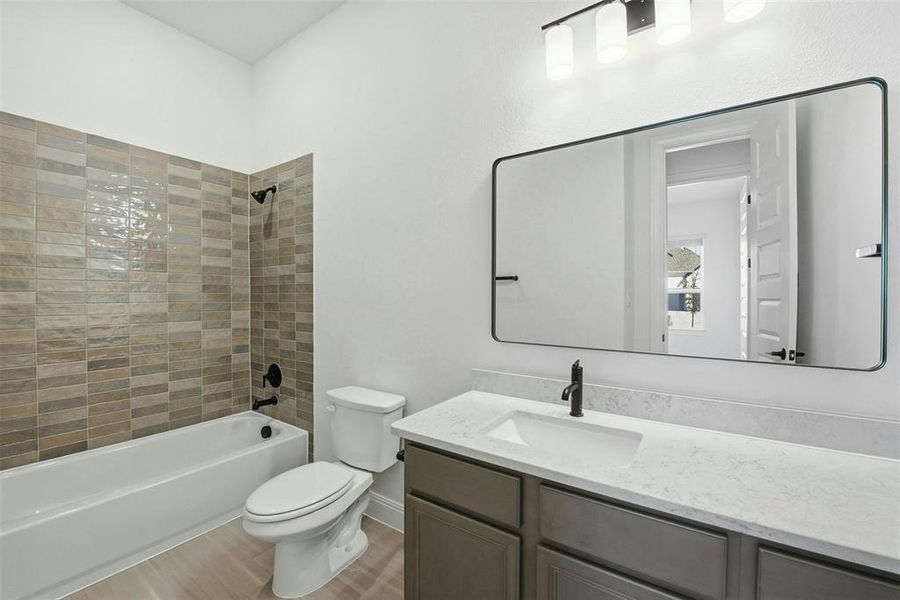 Bathroom featuring a white bathtub, rectangular vanity mirror with a black frame, light wood-finish flooring, built-in vanity with light countertops, and a full tile surround in the shower