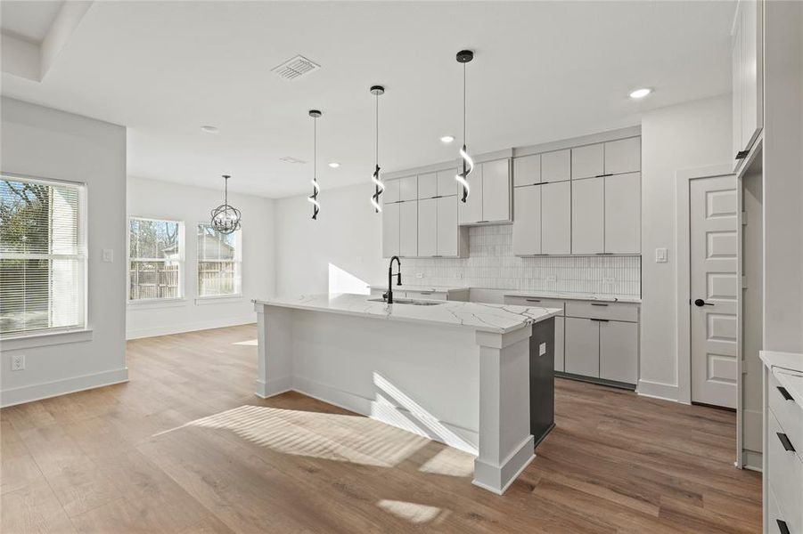 Kitchen with a sink, decorative backsplash, wood finished floors, and an island with sink