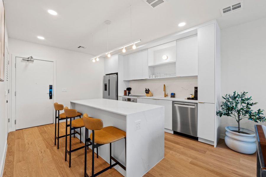 Shown in the Skylark palette, this kitchen features white cabinetry, brass hardware, quartz countertops with subtle veining, and Bosch appliances. Residences come with a fully functional setup including cookware, dishes, and a coffee machine for everyday use. Shown in the Skylark palette, this kitchen features white cabinetry, brass hardware, quartz countertops with subtle veining, and Bosch appliances. Residences come with a fully functional setup including cookware, dishes, and a coffee machine for everyday use.