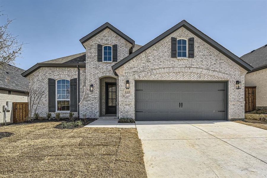 French country home featuring brick siding, fence, concrete driveway, roof with shingles, and a garage