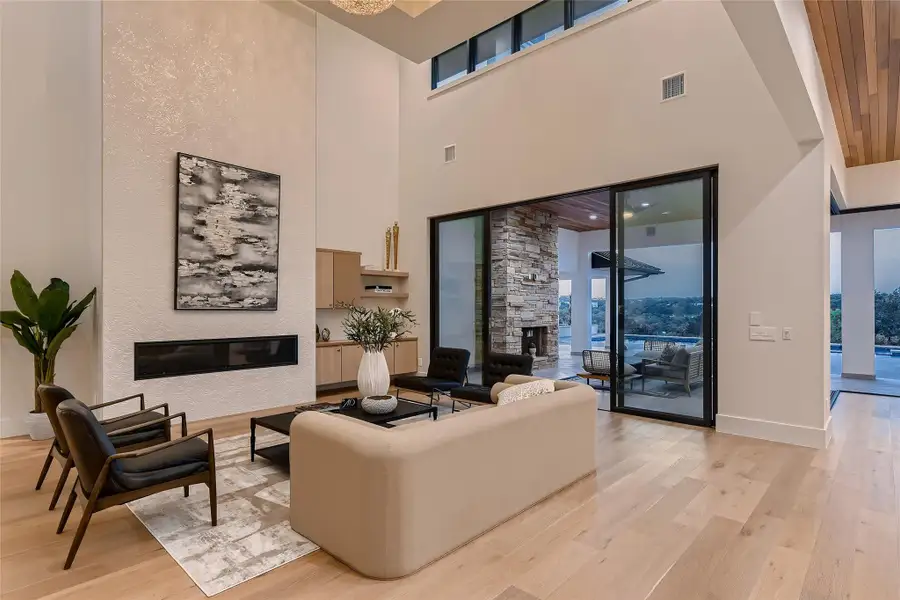 Living room featuring high ceilings, hardwood floors, a linear fireplace, and sliding glass doors that open to an outdoor living area