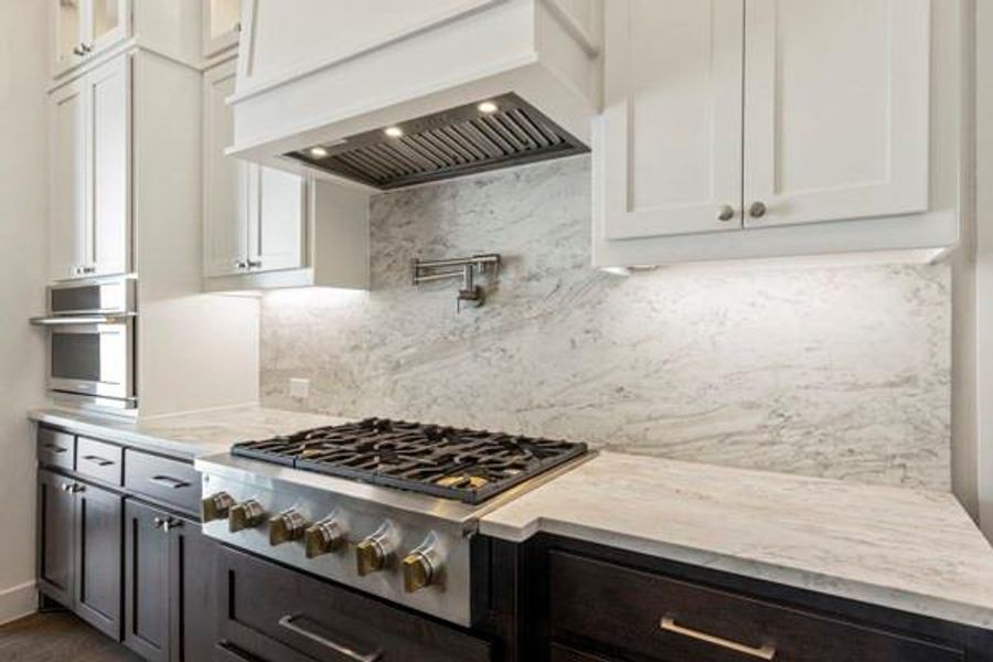 Kitchen with premium range hood, backsplash, stainless steel appliances, white cabinets, and light stone counters Kitchen with premium range hood, backsplash, stainless steel appliances, white cabinets, and light stone counters