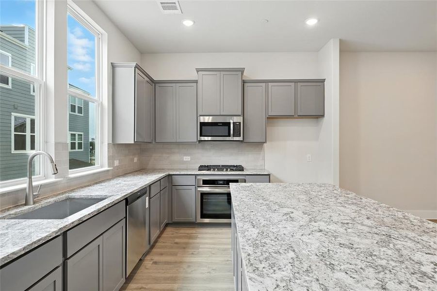 Kitchen with gray cabinetry, light wood-style floors, light stone counters, backsplash, and recessed lighting