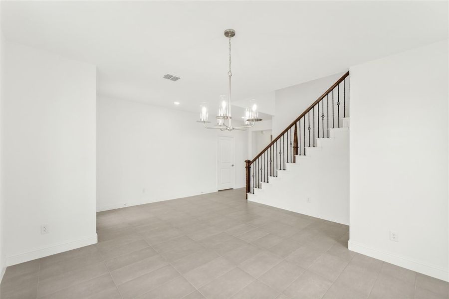 Open living area with gray tile floors, chandelier, and staircase with iron balusters Open living area with gray tile floors, chandelier, and staircase with iron balusters