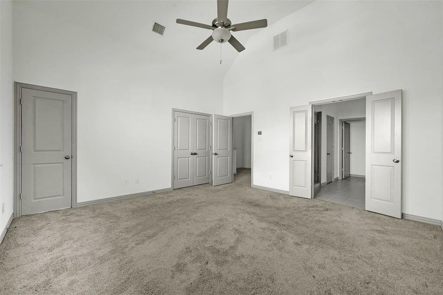 Unfurnished bedroom with high vaulted ceiling, light carpet, ceiling fan, and two closets Unfurnished bedroom with high vaulted ceiling, light carpet, ceiling fan, and two closets