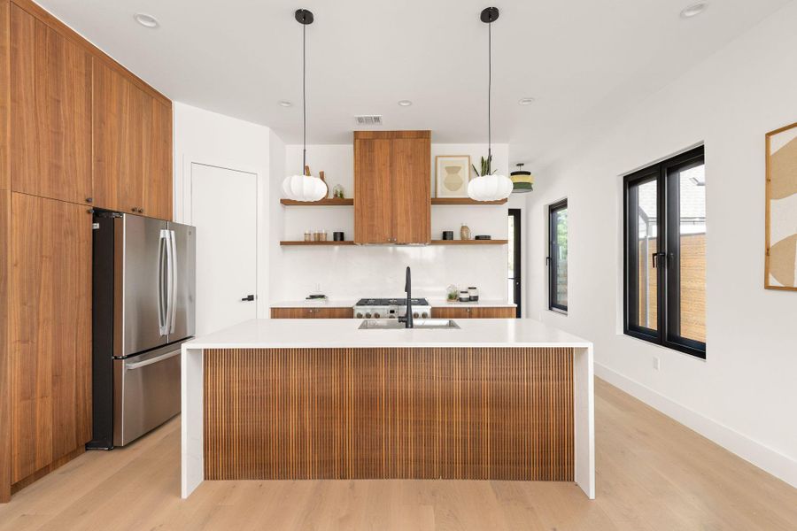 A sleek, contemporary kitchen boasts a spacious island and integrated wood cabinetry for modern living.