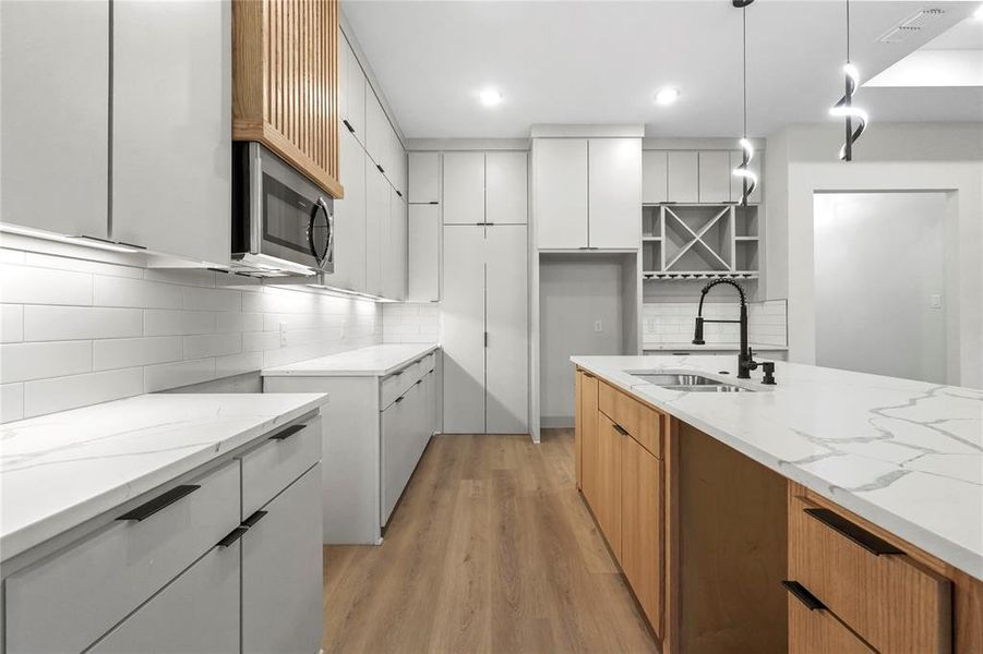 Kitchen with light stone countertops, white cabinetry, backsplash, light wood-style flooring, and recessed lighting