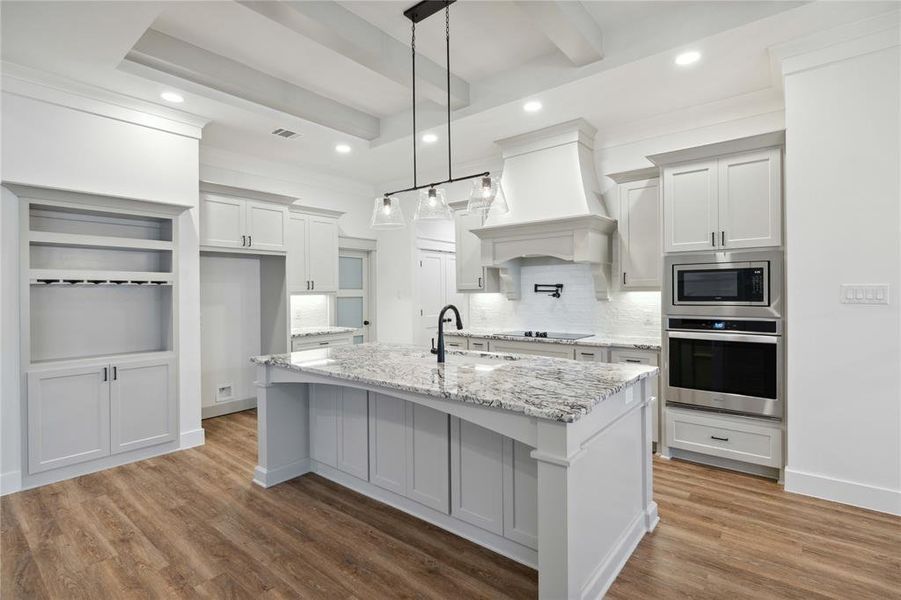 Kitchen with premium range hood, a kitchen island with sink, stainless steel appliances, hardwood / wood-style flooring, and sink