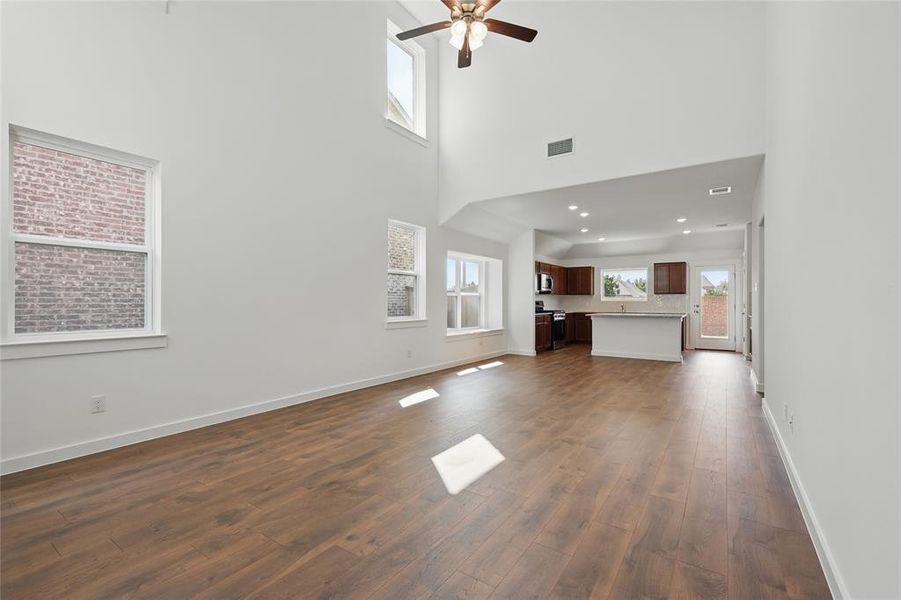 Unfurnished living room featuring healthy amount of natural light, dark wood-style floors, a ceiling fan, and a high ceiling
