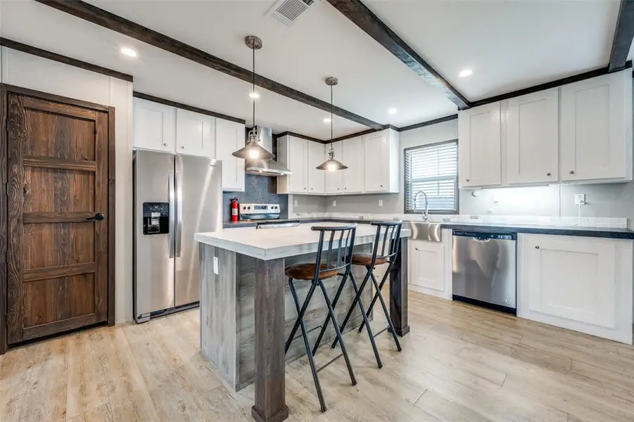 Kitchen featuring stainless steel appliances, white cabinetry, a breakfast bar, and light wood-style flooring Kitchen featuring stainless steel appliances, white cabinetry, a breakfast bar, and light wood-style flooring