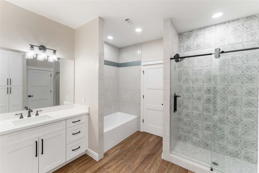 This modern bathroom features a sleek design with a spacious glass-enclosed shower, patterned tile, a separate bathtub, and elegant white cabinetry with black fixtures.