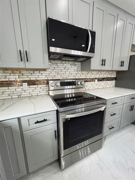 Kitchen featuring light stone countertops, stainless steel appliances, marble finish floor, and gray cabinets Kitchen featuring light stone countertops, stainless steel appliances, marble finish floor, and gray cabinets