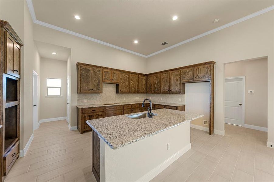 Kitchen featuring a center island with sink, backsplash, light stone counters, and sink