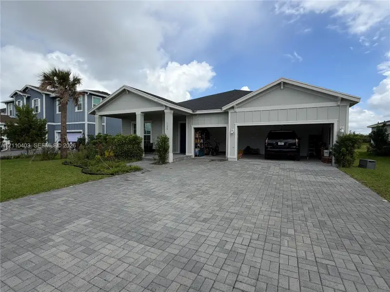 Single-story residence with a light-toned vertical siding exterior, covered front porch, multi-car garage, and paver driveway